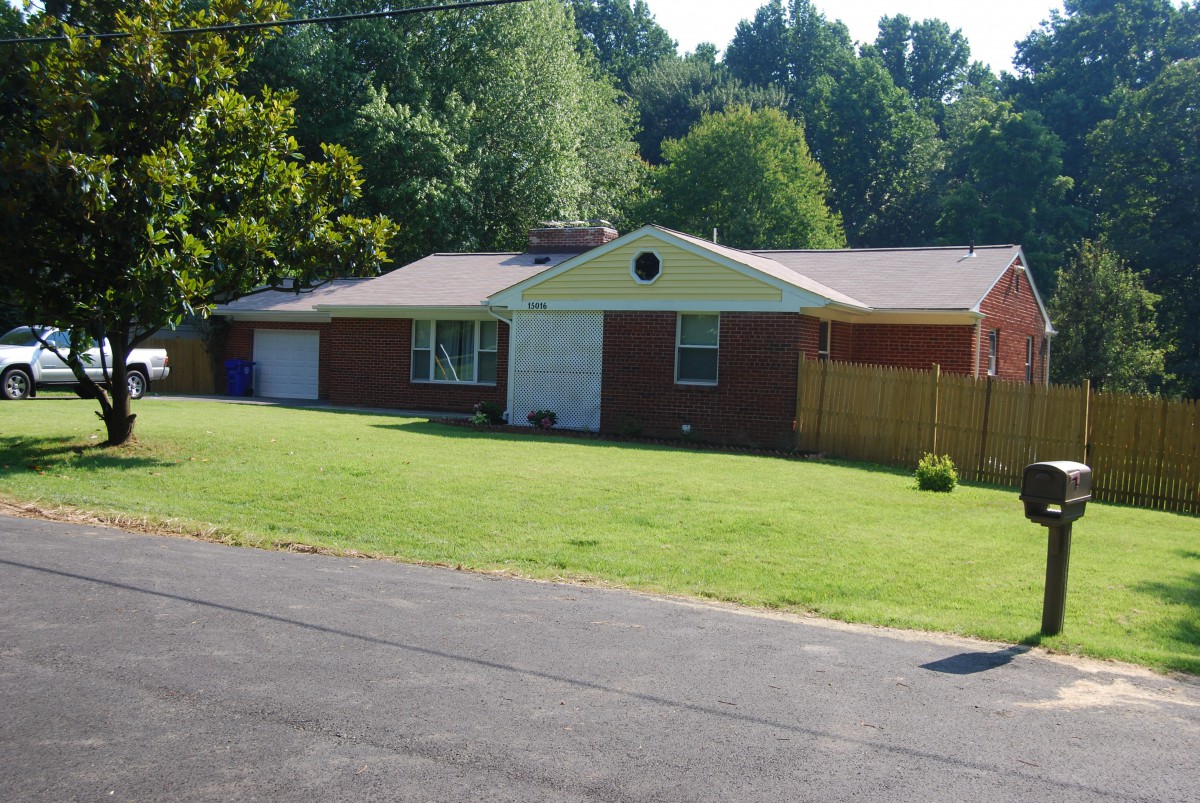 A suburban brick house with a well-maintained lawn and surrounding trees.