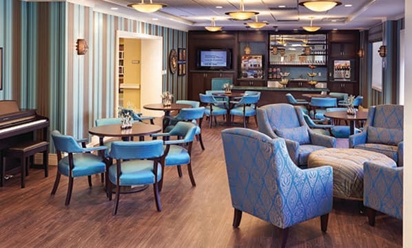 A modern lounge area featuring blue chairs, tables, and a bar with a wooden floor.