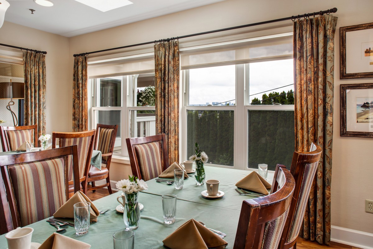A well-set dining table in a bright room with large windows and elegant curtains.