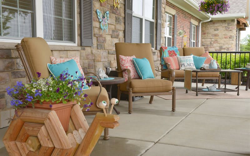 A cozy porch setting with comfortable chairs and colorful cushions, complemented by decorative flowers.