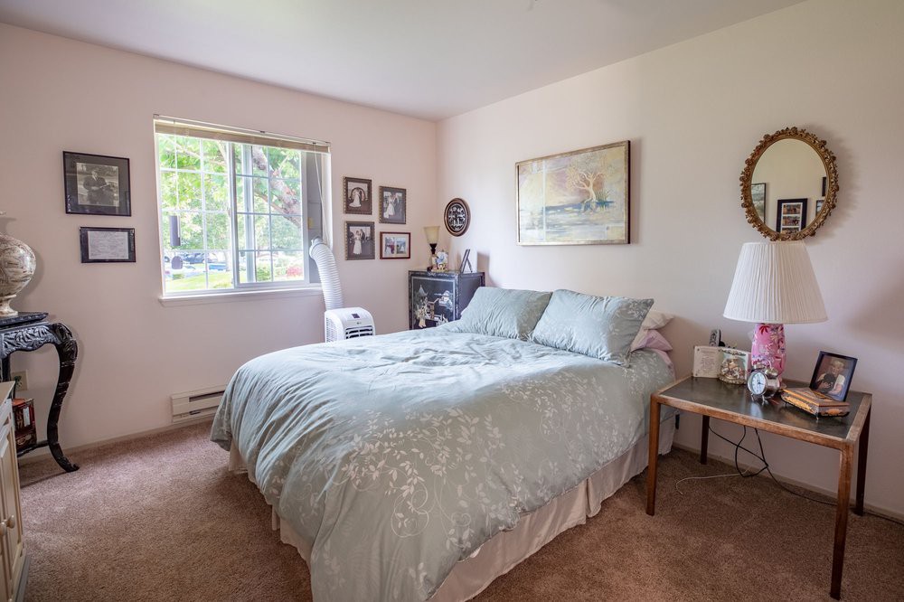 A cozy bedroom features a comfortable bed, artwork on the walls, and natural light streaming through the window.
