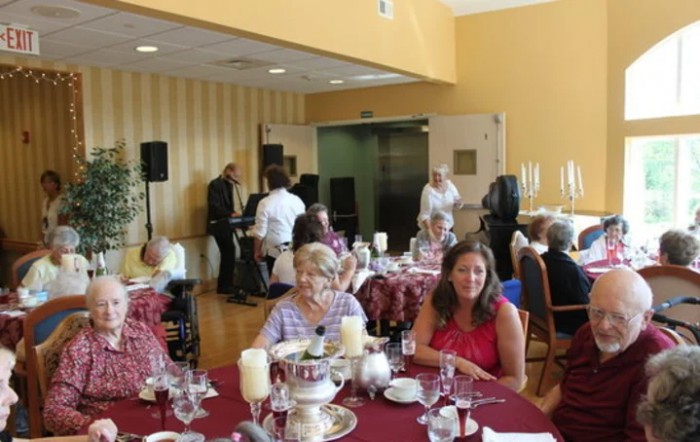 A group of people socializing at a decorated indoor event with dining tables.