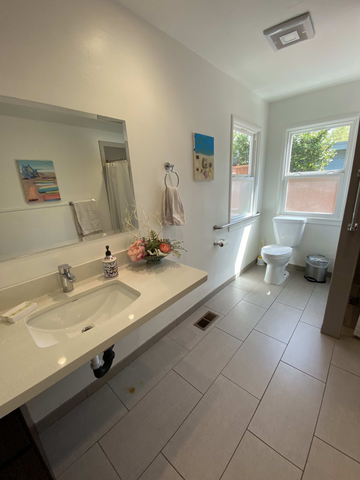 A modern bathroom with a large sink, mirror, and natural light from the window.