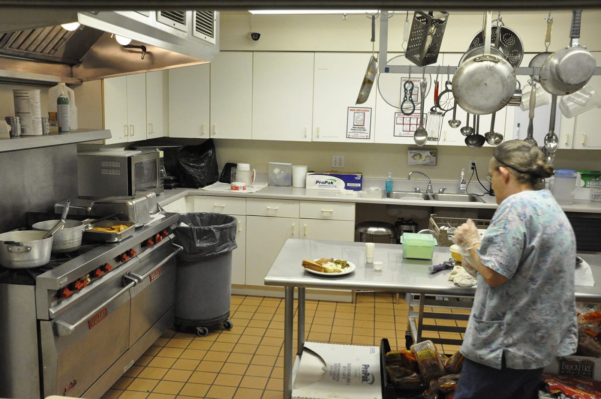 A commercial kitchen with a worker preparing food at a counter.