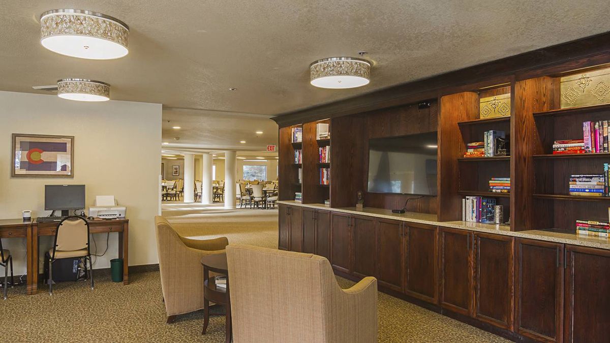 A cozy lounge area with comfortable seating, a TV, bookshelves, and warm ambient lighting.