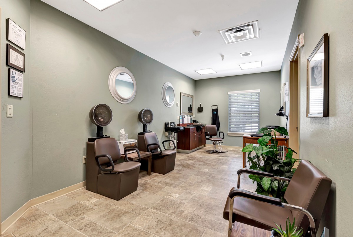 A modern hair salon interior with chairs, hair dryers, and mirrors, featuring bright lighting and greenery.