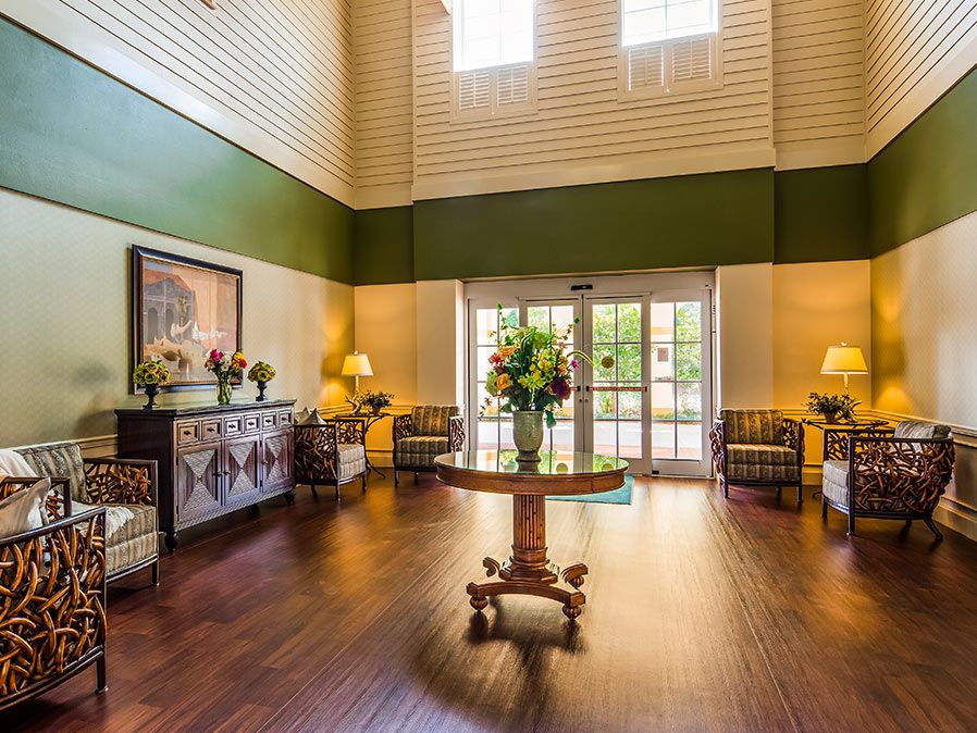 A spacious and elegantly decorated lobby with wooden floors, featuring a central table adorned with flowers, surrounded by comfortable seating and warm lighting.