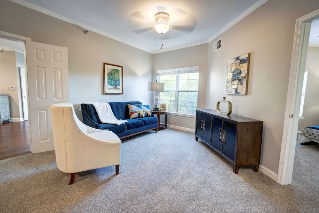 A cozy living room featuring a blue sofa, white armchair, and decorative artwork.