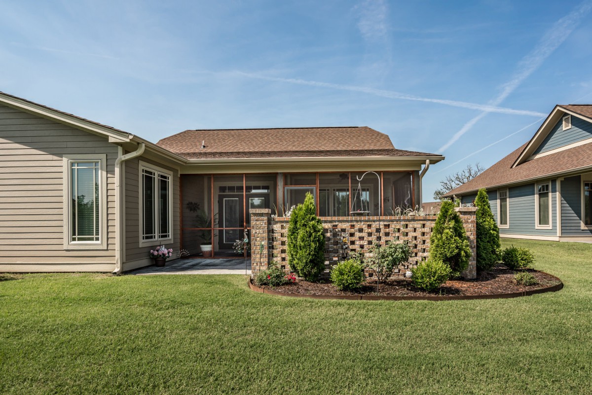 A well-maintained backyard featuring a lush green lawn and a charming house with a small garden.