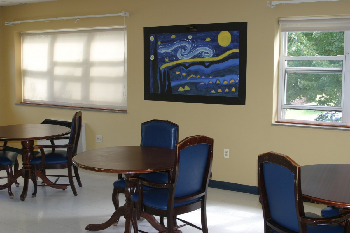 A room with a round table and chairs, featuring a painting on the wall.