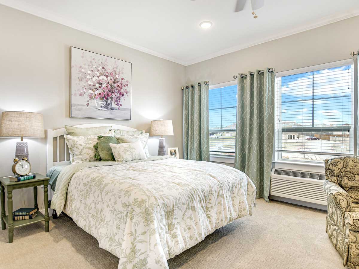 A cozy and well-lit bedroom with a large bed, soft bedding, and a nature painting above the headboard.