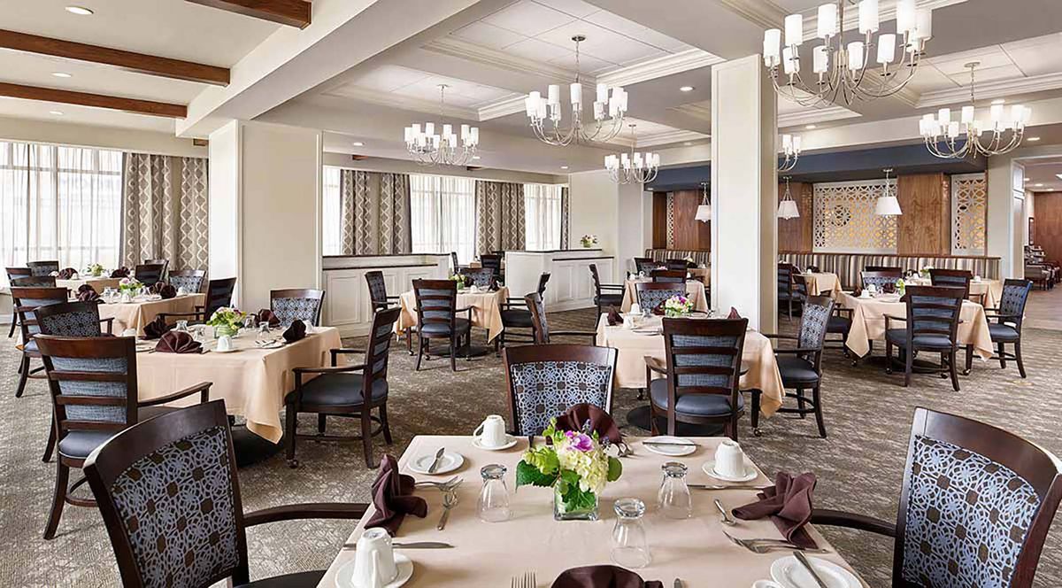 An elegant dining room with neatly arranged tables and chairs, adorned with chandeliers.