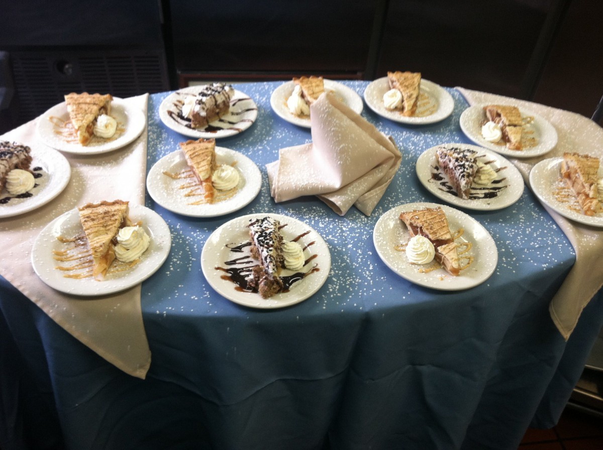 A table set with plates of pie and ice cream, some topped with chocolate drizzle and whipped cream.