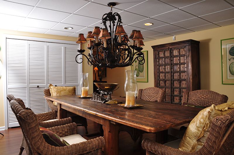 A cozy dining room featuring a large wooden table, rattan chairs, and an ornate chandelier.