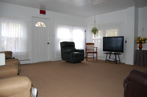 A cozy living room featuring a recliner, a small chair, a television, and natural light from the windows.