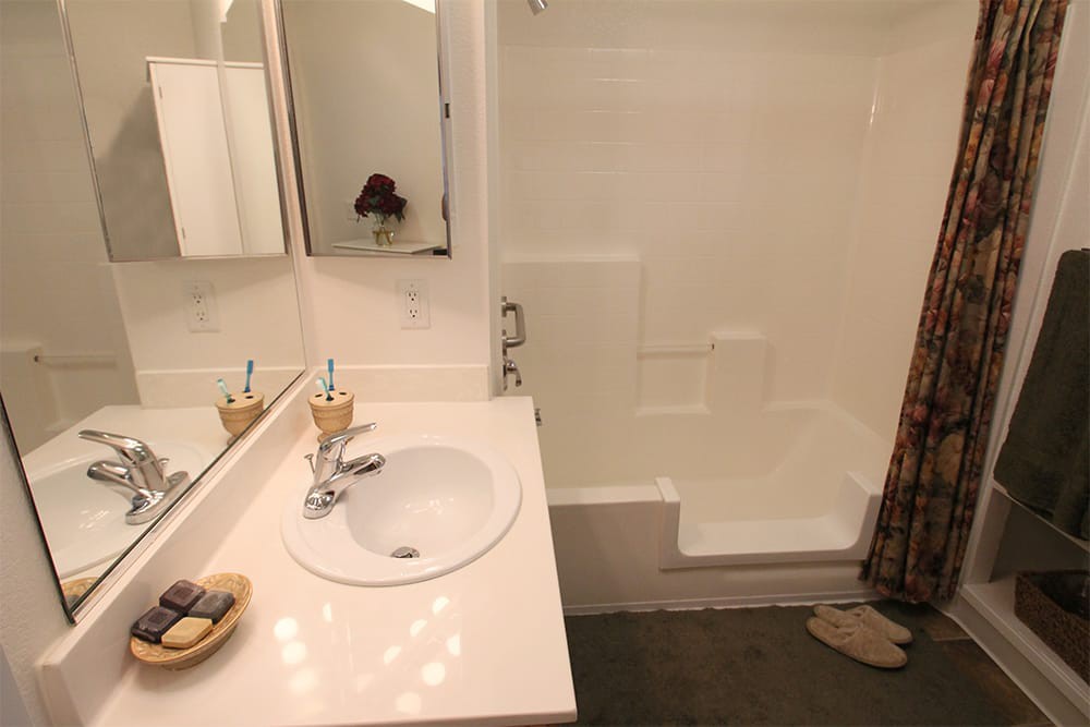 A clean white bathroom featuring a sink, mirror, and shower.