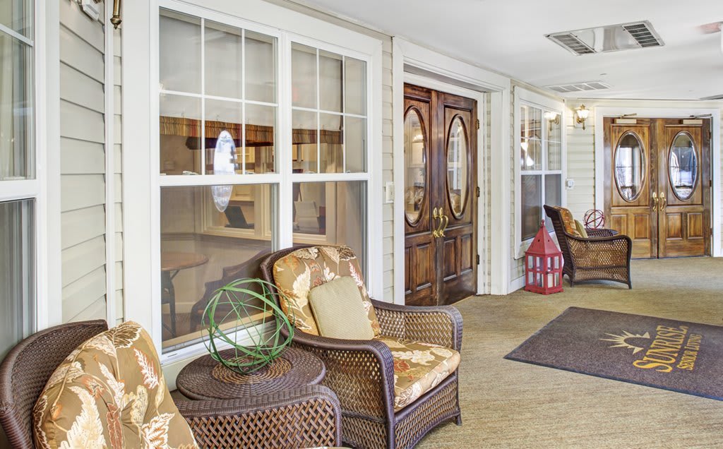 A cozy porch with wicker furniture and decorative elements, featuring a wooden front door.