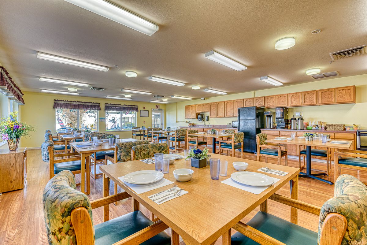 A spacious dining area with wooden tables and chairs, adjacent to a kitchen.