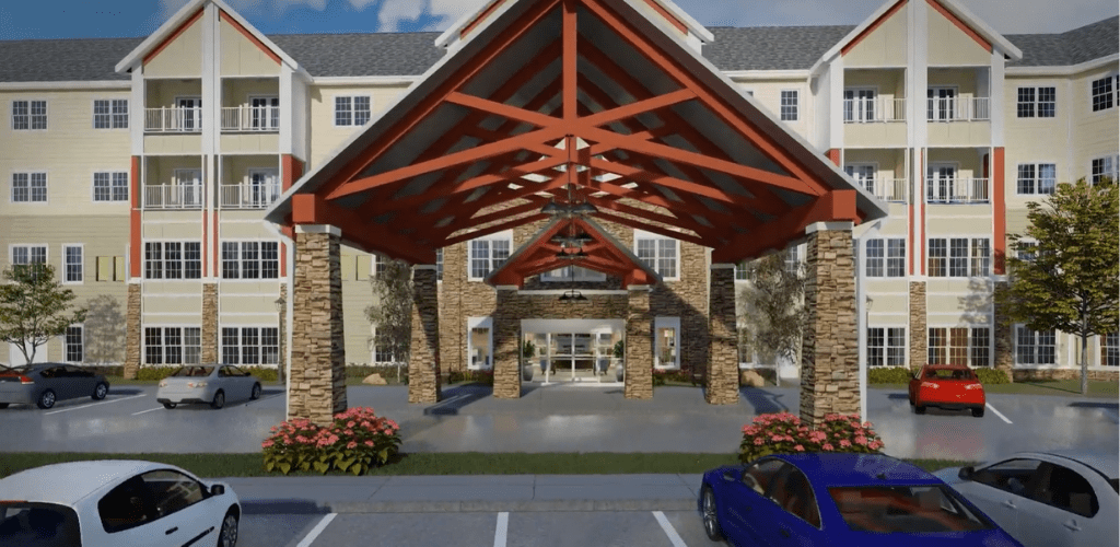 The image shows the entrance of a building with a large awning, parking area, and landscaped surroundings.
