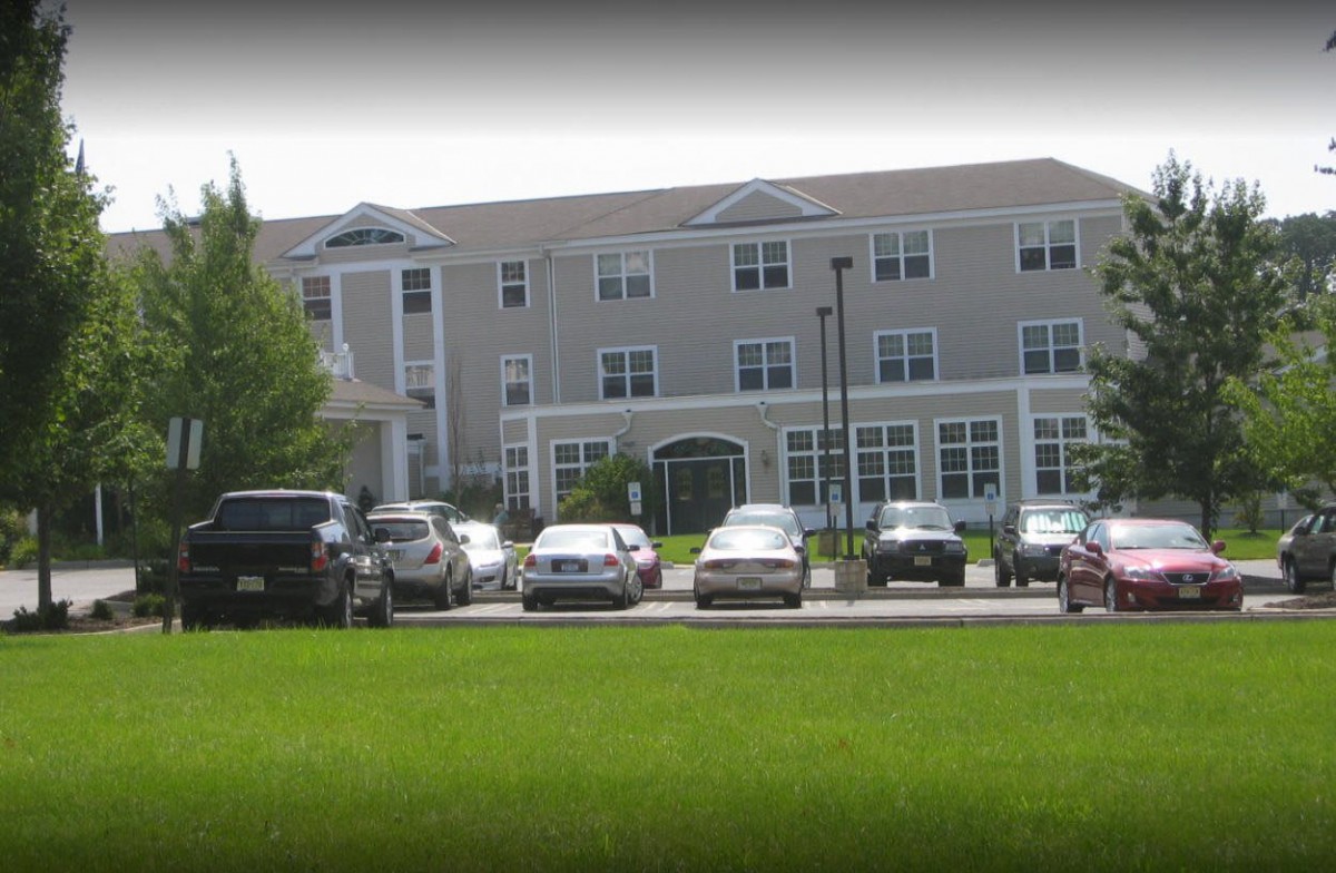 A residential building with a parking lot in front and a grassy lawn.