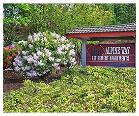 Entrance sign for Alpine West Retirement Apartments surrounded by lush greenery and blooming flowers.