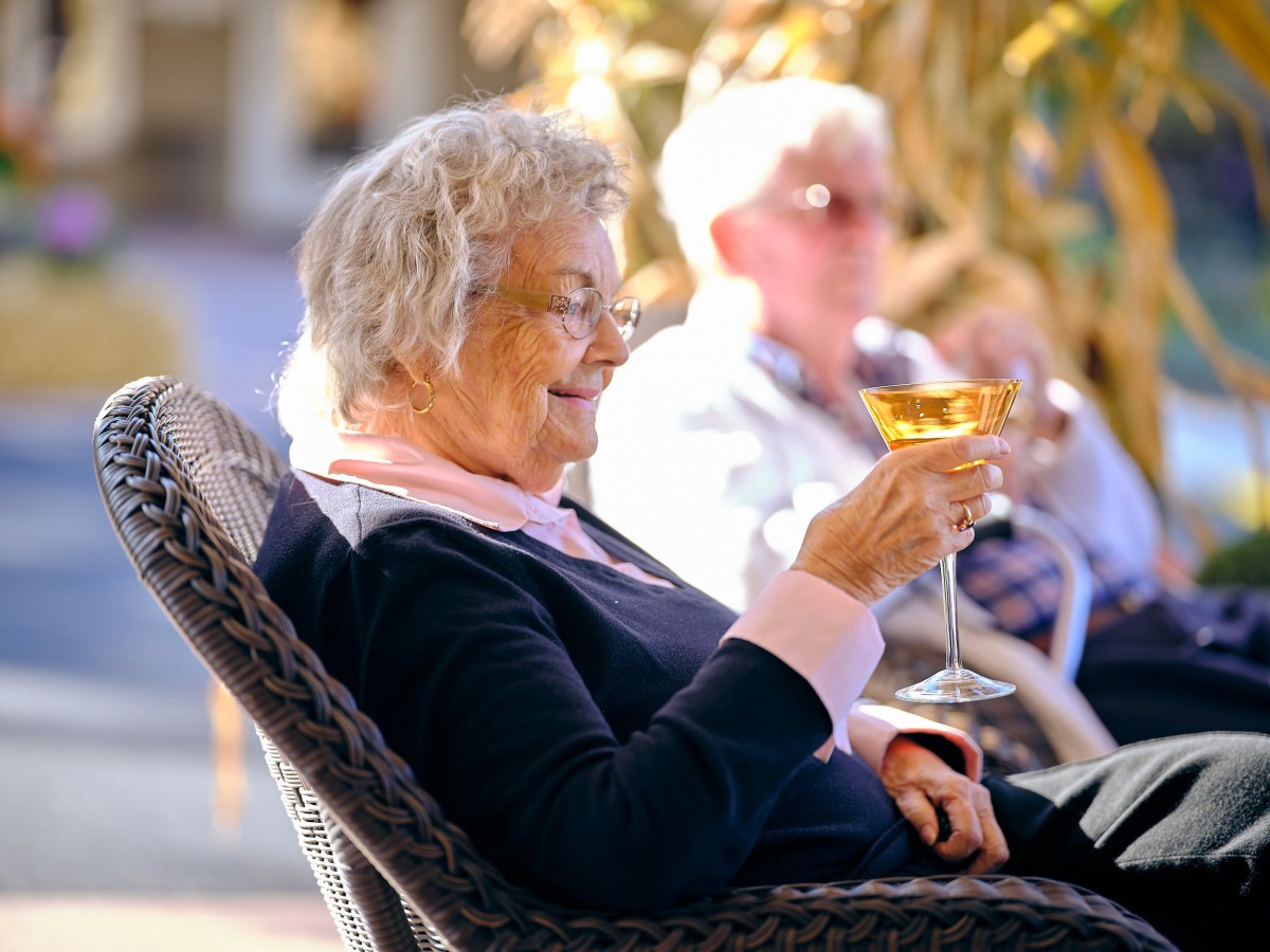 An elderly woman enjoys a drink while relaxing outside.