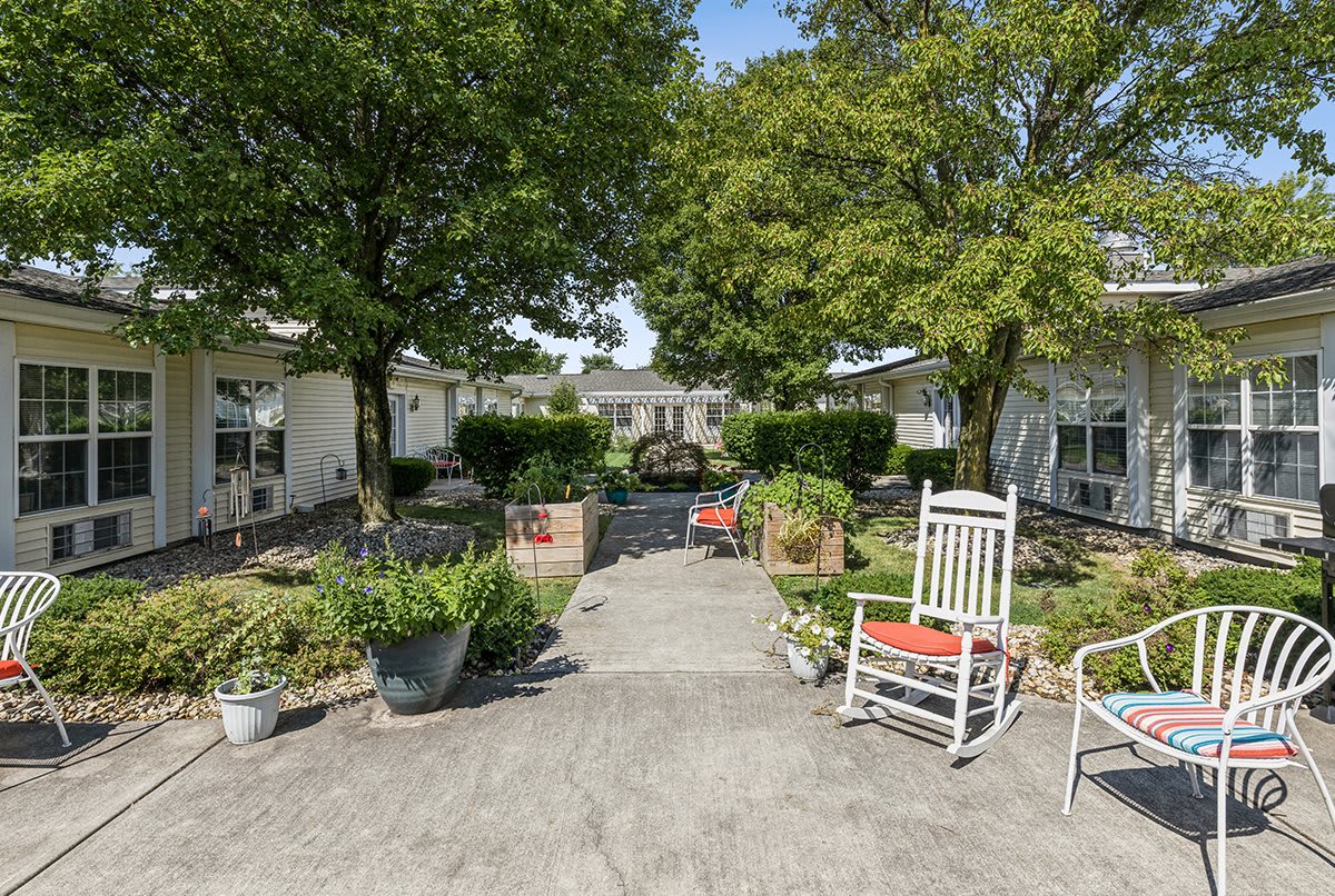 A peaceful courtyard with a pathway, surrounded by trees and seating areas.