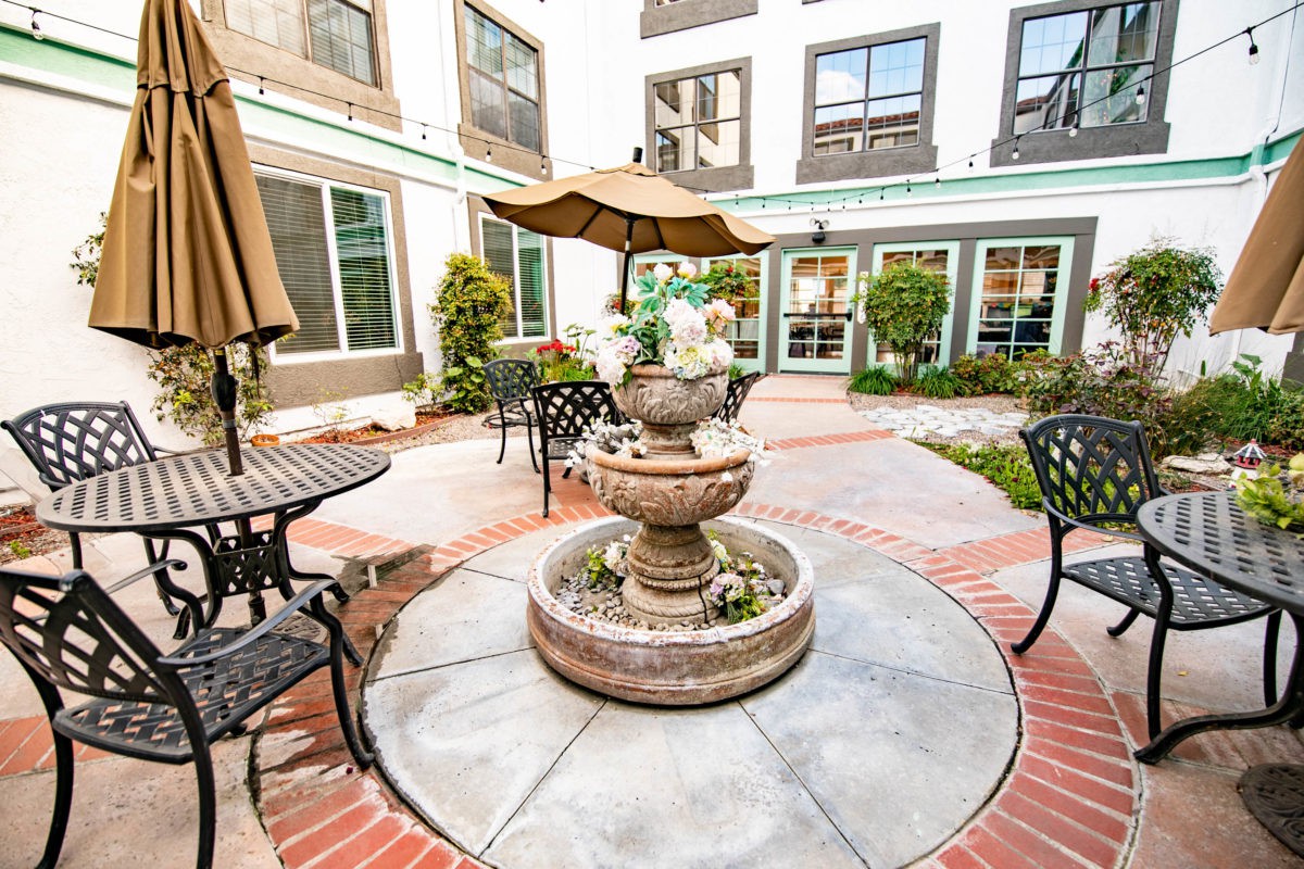 A charming courtyard featuring a central fountain surrounded by tables and chairs with umbrellas.