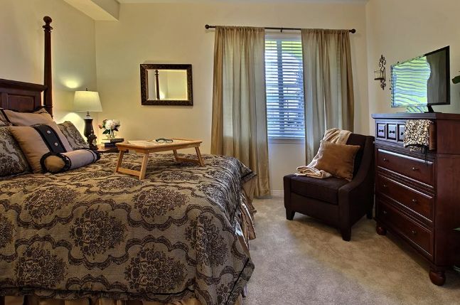 A cozy bedroom with patterned bedding, a comfortable chair, and a small table on the bed.