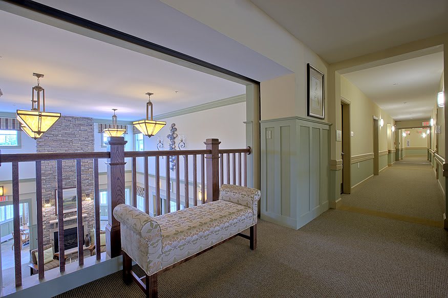 A hallway with a bench overlooking the stairs and well-lit interior.