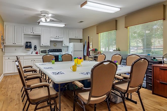 A multi-purpose meeting room with a conference table, surrounded by chairs and adjacent to a kitchen area.