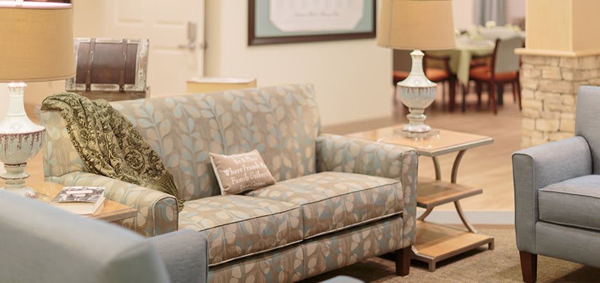 A cozy living room setup featuring a patterned sofa, side table with a lamp, and decorative cushions.