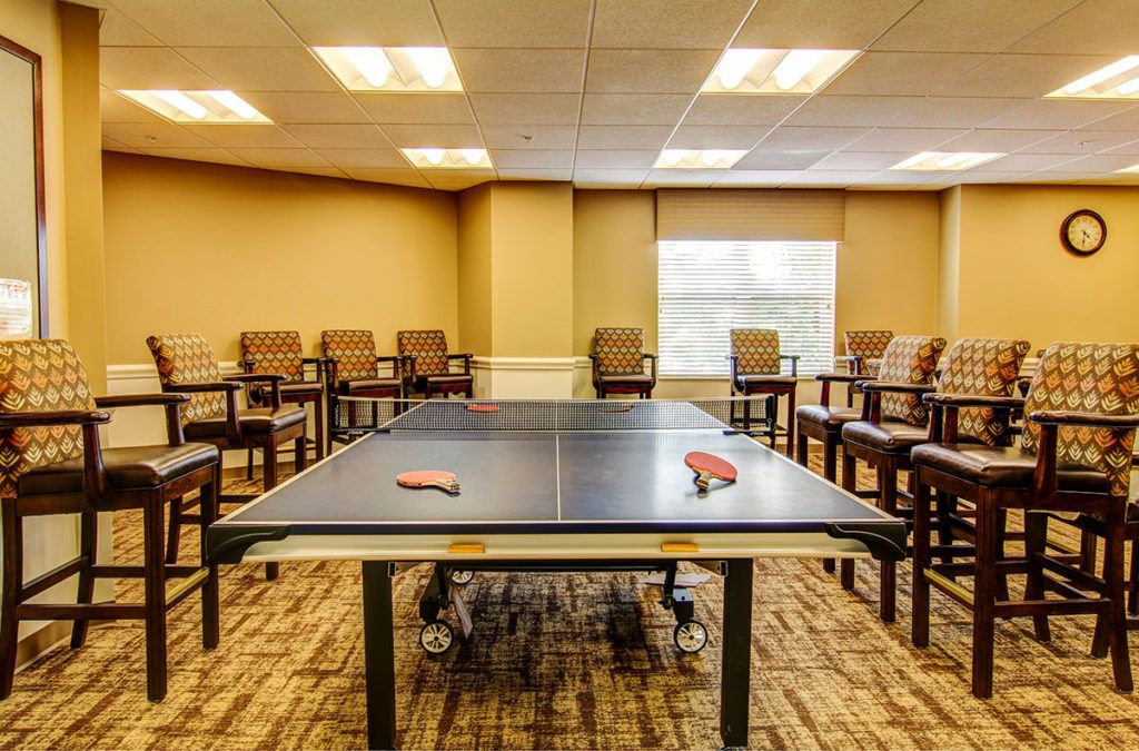 An indoor leisure room featuring a ping pong table with paddles placed on it, surrounded by chairs.