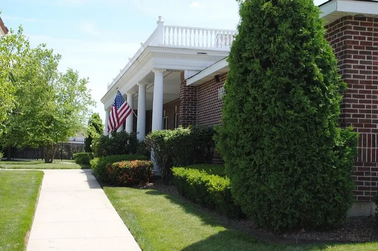 A brick building with columns and an American flag, surrounded by greenery and a well-maintained lawn.