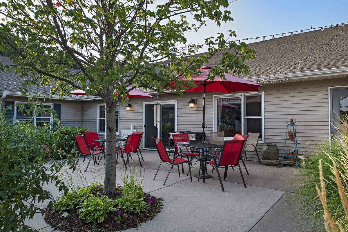 A cozy residential patio with red chairs and umbrellas, surrounded by plants.