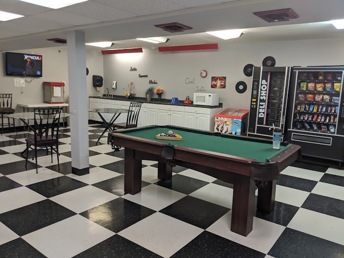A modern game room featuring a pool table and a checkered floor with a vending machine in the background.