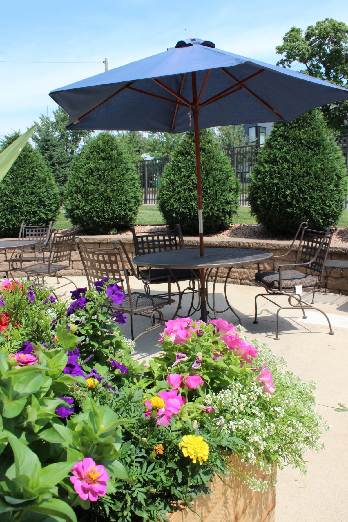 A beautifully arranged outdoor patio with colorful flowers, metal furniture, and a large umbrella.