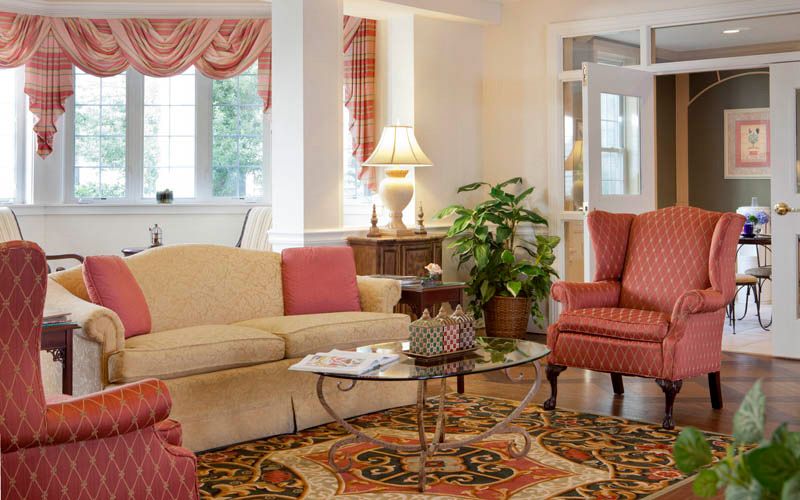 A cozy living room with a beige sofa, red armchairs, a glass coffee table, and decorative elements such as a lamp and an indoor plant.