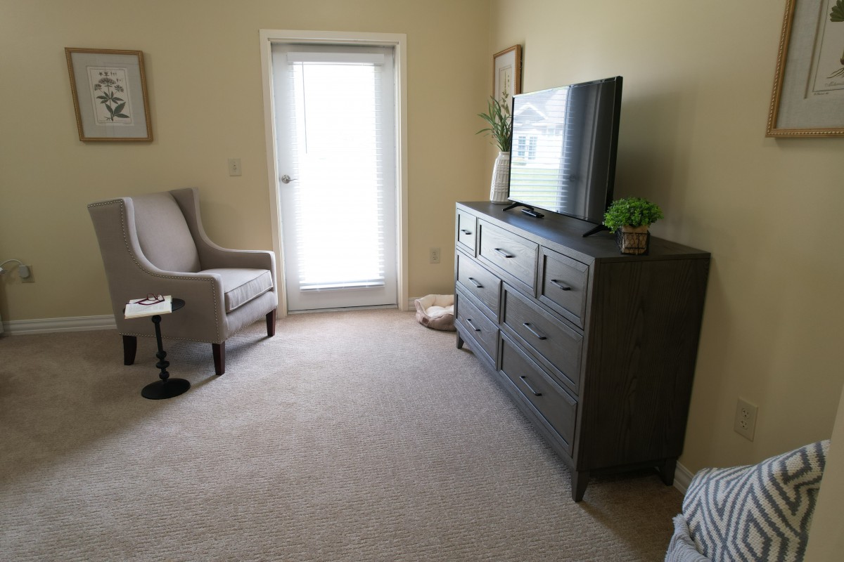A cozy living room with a television, armchair, and dresser.