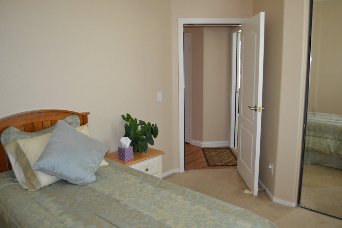 A cozy bedroom with a bed, nightstand, plant, and an open door leading to a hallway.