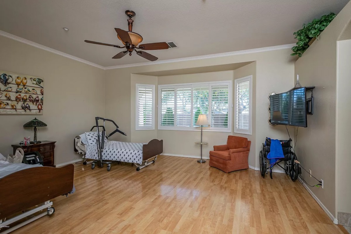 A spacious bedroom with a hospital bed, hardwood flooring, and a ceiling fan.