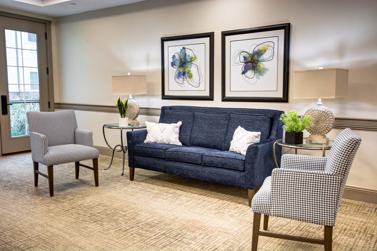 A modern living room with a blue sofa, patterned chairs, and framed artwork on the wall.