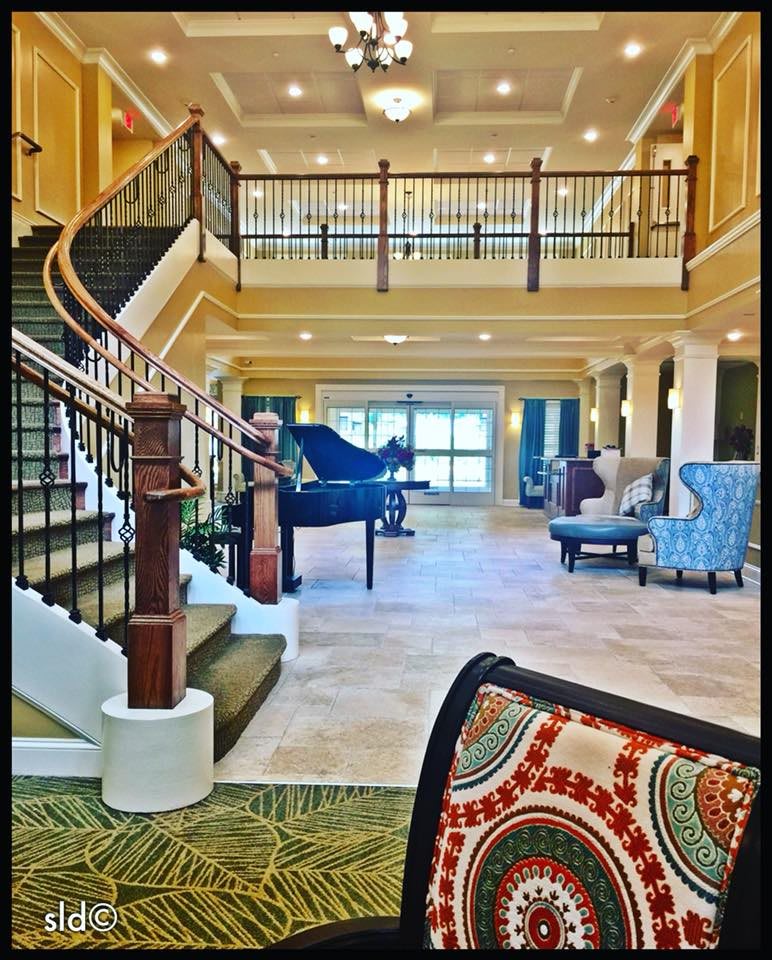 A spacious lobby featuring a grand piano, elegant staircase, and comfortable seating area.