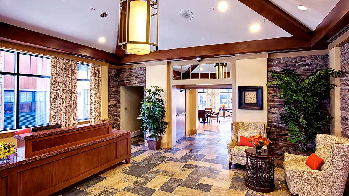 A modern lobby featuring stone walls, wooden furniture, and bright lighting with decorative plants.