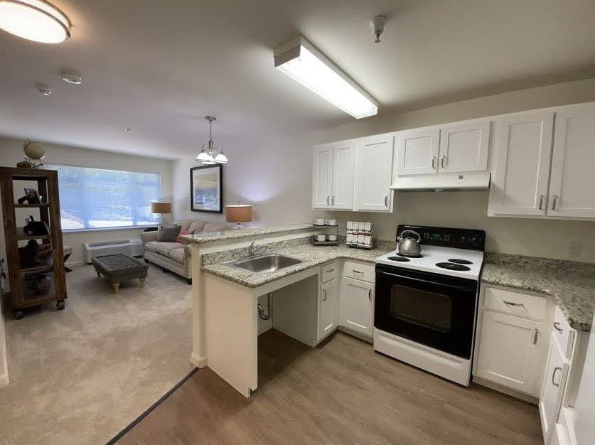 A modern open-layout apartment featuring a kitchen with white cabinets and a connected living room.