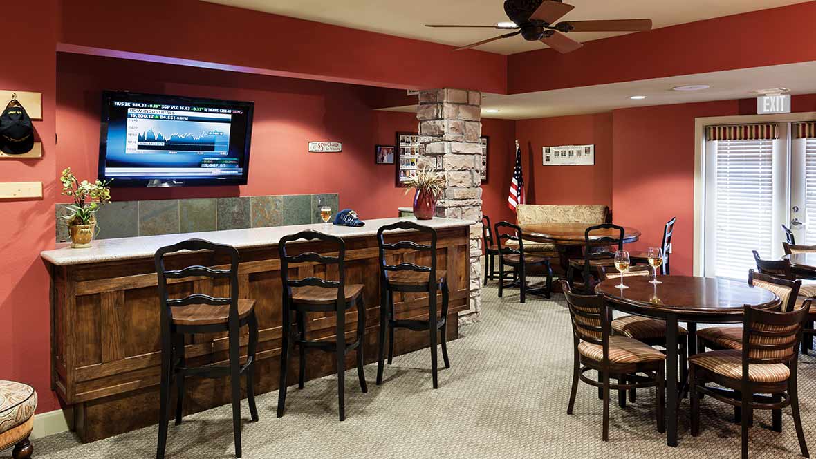 A cozy bar with wooden chairs, tables, and a television against a brick accent wall.