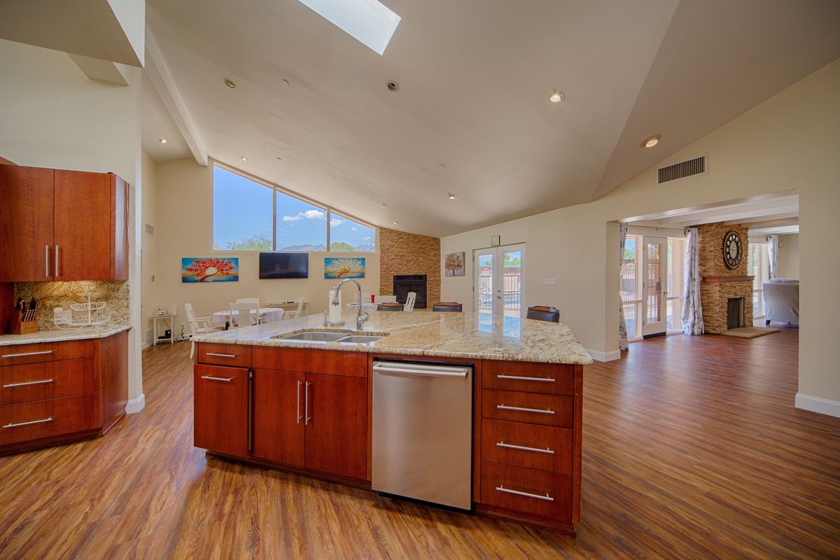 A modern, open-concept kitchen featuring an island counter and wood flooring, illuminated by natural light from large windows and a skylight.