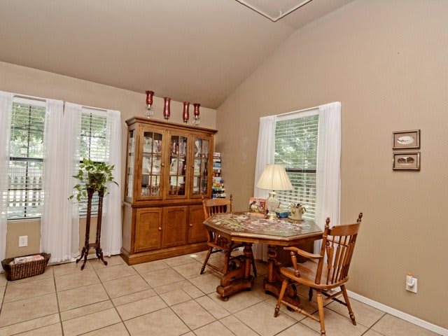 A cozy dining area featuring a round table with wooden chairs and a china cabinet, illuminated by natural light through the windows.