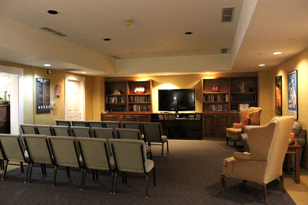 A well-lit conference room with rows of chairs facing a television and bookshelves.