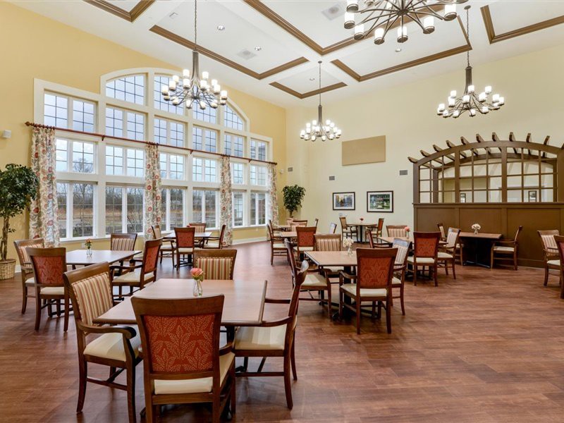 A spacious and elegant dining hall with large windows, wooden floors, and decorative chandeliers.